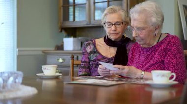 Yaşlı, gülümseyen, mutlu bir kadın eski fotoğraflara bakıyor ve yemek masasındaki kızımızla ilgili anıları hatırlıyor..
