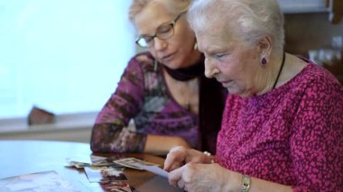 Yaşlı kadın kızıyla fotoğraflara bakıyor. Kıdemli kadın yemek odasında oturmuş kızıyla fotoğraflarına bakıyor. Beyin eğitimi. Bellek etkinliği.