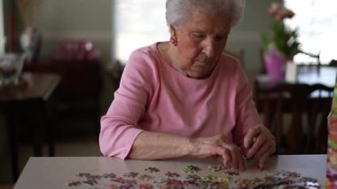 Mutlu yaşlı yaşlı bir kadın evde yapboz üzerinde çalışıyor..