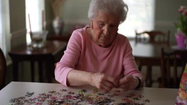 Mutlu yaşlı yaşlı bir kadın evde yapboz üzerinde çalışıyor..