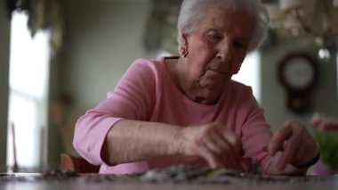 Neşeli, yaşlı, yaşlı bir kadının evde yapboz üzerinde çalışmasının düşük açılı görüntüsü.