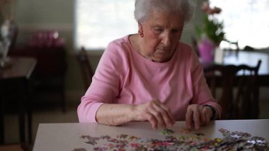 Neşeli yaşlı yaşlı yaşlı bir kadın evde yapboz üzerinde çalışıyor..