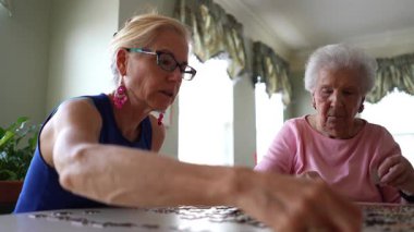 Gülümseyen olgun kadın yapboz parçalarını yerleştirirken yaşlı bayan yapboz parçalarını hareket ettiriyor. Sevdiklerinle vakit geçirme kavramı.