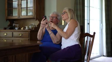 Yemek odasında yaşlı bir kadın ve yetişkin bir kız gözlüklü ve akıllı telefonlara bakarak eğleniyorlar..