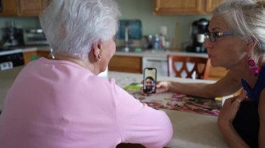 Mutlu gülümseyen, olgun orta yaşlı kızı olan yaşlı bir kadın oğluyla telefonda görüntülü konuşma yapıyor. Gülümseyen sarışın akıllı telefondan ailenle konuşuyor..