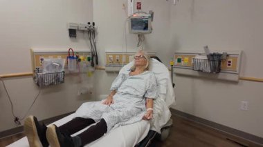 Winchester, VA, USA - 09 03 2025: A mature woman is resting on a hospital bed, wearing a patient gown with medical equipment in the background, depicting her recovery journey.