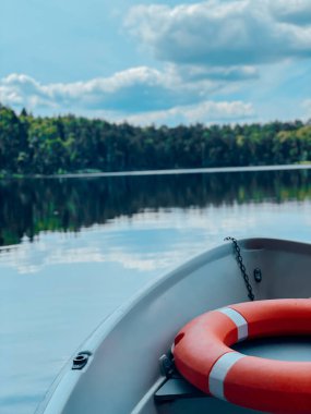 Sakin bir gölde yüzen sakin bir tekne, berrak mavi gökyüzünün altında yemyeşil, güzel bir ormanla çevrili. Sahne doğanın huzurunu yakalıyor, açık hava macerası, rahatlama ve doğal güzellik temaları için mükemmel..