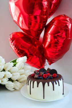 Beyaz lalelerin olduğu bir Sevgililer Günü sahnesi, üstünde yabanmersinleri olan güzel bir pasta, ve kırmızı kalp şeklinde balonlar. 14 Şubat 'ta aşkı zarif bir şekilde kutlamak için mükemmel.