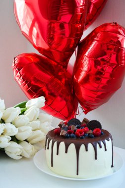 Beyaz lalelerin olduğu bir Sevgililer Günü sahnesi, üstünde yabanmersinleri olan güzel bir pasta, ve kırmızı kalp şeklinde balonlar. 14 Şubat 'ta aşkı zarif bir şekilde kutlamak için mükemmel.