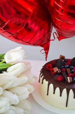 Beyaz lalelerin olduğu bir Sevgililer Günü sahnesi, üstünde yabanmersinleri olan güzel bir pasta, ve kırmızı kalp şeklinde balonlar. 14 Şubat 'ta aşkı zarif bir şekilde kutlamak için mükemmel.