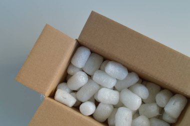 Koruyucu ambalaj malzemeleriyle dolu karton bir kargo kutusu, çevre dostu kağıt dolgu malzemesi ve biyolojik olarak çözünebilir fıstık paketleri de dahil. Bu malzemeler güvenli bir şekilde paketlemek, kırılgan eşyaları korumak ve güvenli bir şekilde teslim etmek için idealdir.