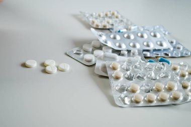 Farklı şekillerde, boyutlarda ve beyaz bir yüzeye dağılmış çeşitli ilaç hapları ve kapsüller. Bu tıbbi konsept sağlık, tedavi, reçeteli ilaçlar ve reçetesiz ilaçları temsil ediyor. Görüntü modayı simgeler