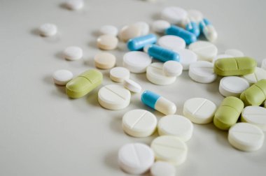 Farklı şekillerde, boyutlarda ve beyaz bir yüzeye dağılmış çeşitli ilaç hapları ve kapsüller. Bu tıbbi konsept sağlık, tedavi, reçeteli ilaçlar ve reçetesiz ilaçları temsil ediyor. Görüntü modayı simgeler