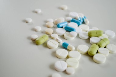 Farklı şekillerde, boyutlarda ve beyaz bir yüzeye dağılmış çeşitli ilaç hapları ve kapsüller. Bu tıbbi konsept sağlık, tedavi, reçeteli ilaçlar ve reçetesiz ilaçları temsil ediyor. Görüntü modayı simgeler