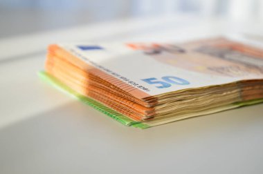 Çoğunluğu 50 Euro 'luk banknotlardan oluşan bir deste, beyaz bir masaya düzgünce yerleştirilmiş. Görüntü finansal istikrar, nakit işlemleri ve zenginlik yönetimini temsil ediyor. Bankacılık, tasarruf, yatırım ve ekonomiyle ilgili kavramların resmedilmesi için ideal