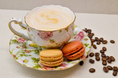 Çok güzel dizayn edilmiş, kremalı kahveyle dolu bir çay fincanı. Yanında da çiçekli bir çay tabağı. Dağınık kahve çekirdekleri sıcacık ve aromatik atmosfere ekleniyor. Bu zarif kompozisyon rel 'in özünü yakalar