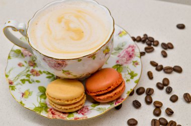 Çok güzel dizayn edilmiş, kremalı kahveyle dolu bir çay fincanı. Yanında da çiçekli bir çay tabağı. Dağınık kahve çekirdekleri sıcacık ve aromatik atmosfere ekleniyor. Bu zarif kompozisyon rel 'in özünü yakalar