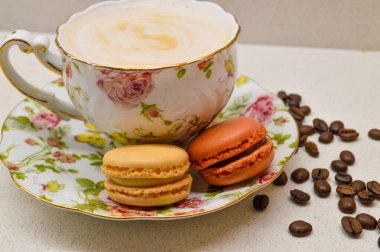 Çok güzel dizayn edilmiş, kremalı kahveyle dolu bir çay fincanı. Yanında da çiçekli bir çay tabağı. Dağınık kahve çekirdekleri sıcacık ve aromatik atmosfere ekleniyor. Bu zarif kompozisyon rel 'in özünü yakalar