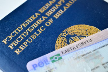 Polonya ikamet kartı (Karta Pobytu) ile birlikte temiz beyaz bir yüzeye yerleştirilmiş Belarus pasaportunun yakın plan görüntüsü. Bu fotoğraf göçmenlik, yasal ikamet, sınır ötesi kimlik ve yabancı Nat 'ın durumunu simgeliyor.