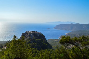 Monolithos Kalesi 'nin nefes kesici panoramik çekimi, Yunanistan' ın Rodos adasında çekilen ışıltılı Ege Denizi 'ne bakan kayalık bir tepenin üzerine tünemişti. Bereketli yeşil çam ormanları ve engebeli kıyı şeridi ile çevrili bu ortaçağ kalesi,