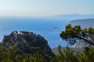 Monolithos Kalesi 'nin nefes kesici panoramik çekimi, Yunanistan' ın Rodos adasında çekilen ışıltılı Ege Denizi 'ne bakan kayalık bir tepenin üzerine tünemişti. Bereketli yeşil çam ormanları ve engebeli kıyı şeridi ile çevrili bu ortaçağ kalesi,