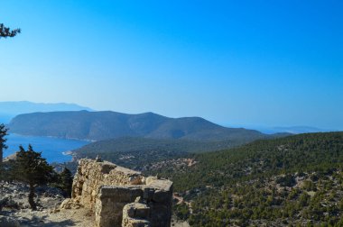 Monolithos Kalesi 'nin nefes kesici panoramik çekimi, Yunanistan' ın Rodos adasında çekilen ışıltılı Ege Denizi 'ne bakan kayalık bir tepenin üzerine tünemişti. Bereketli yeşil çam ormanları ve engebeli kıyı şeridi ile çevrili bu ortaçağ kalesi,