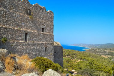 Yunanistan 'ın Rodos kentindeki antik Monolithos Şatosu' nun bir bölümünde, bu resim, arka planda Ege Denizi 'ni ve kıyı şeridini süpüren bereketli bir ormanın üzerinde duran kalenin yıpranmış taş duvarlarını yakalıyor. S Şövalyeleri tarafından inşa edildi.