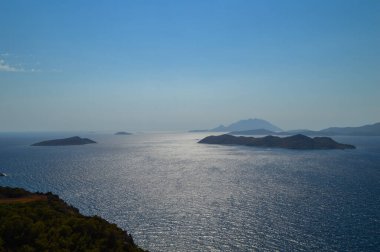 Yunanistan 'ın Rodos kıyı şeridi boyunca uzanan derin mavi Ege Denizi' nin nefes kesici manzarası. Sahne engebeli kayalıklar ve vahşi Akdeniz bitkileri tarafından çerçevelenmiş, gözü denizin gökyüzü ile buluştuğu sakin ufka götürüyor. Mesafe