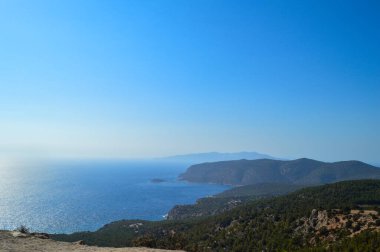 Yunanistan 'ın Rodos kıyı şeridi boyunca uzanan derin mavi Ege Denizi' nin nefes kesici manzarası. Sahne engebeli kayalıklar ve vahşi Akdeniz bitkileri tarafından çerçevelenmiş, gözü denizin gökyüzü ile buluştuğu sakin ufka götürüyor. Mesafe