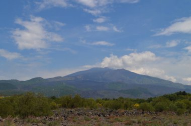 İtalya 'nın Sicilya kentindeki Etna Dağı' nın volkanik yamaçlarının manzarası. Siyah lav kayaları, seyrek bitki örtüsü ve canlı mavi gökyüzü patlamalarla şekillenen dramatik bir doğal manzara yaratır..