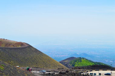 İtalya 'nın Sicilya kentindeki Etna Dağı' nın volkanik yamaçlarının manzarası. Siyah lav kayaları, seyrek bitki örtüsü ve canlı mavi gökyüzü patlamalarla şekillenen dramatik bir doğal manzara yaratır..