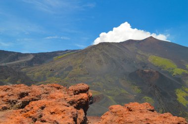 İtalya 'nın Sicilya kentindeki Etna Dağı' nın volkanik yamaçlarının manzarası. Siyah lav kayaları, seyrek bitki örtüsü ve canlı mavi gökyüzü patlamalarla şekillenen dramatik bir doğal manzara yaratır..