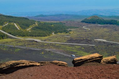 İtalya 'nın Sicilya kentindeki Etna Dağı' nın volkanik yamaçlarının manzarası. Siyah lav kayaları, seyrek bitki örtüsü ve canlı mavi gökyüzü patlamalarla şekillenen dramatik bir doğal manzara yaratır..