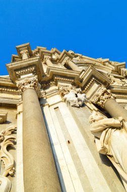 Gösterişli taş oymalar, klasik sütunlar ve canlı mavi gökyüzüne karşı heykel detaylarının yer aldığı barok katedral cephesinin dramatik düşük açılı görüntüsü. Mimarlık ve seyahat içeriği için mükemmel