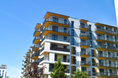 Temiz bir gökyüzünün altında canlı balkonları olan modern yerleşim tesislerinin dinamik görüntüsü. Varşova 'da aktif gayrimenkul gelişimini ve yeni yaşam fırsatlarını yansıtıyor.