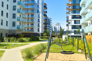 Canlı, çağdaş bir oyun alanı. Salıncak ve ahşap oyun yapıları, yemyeşil peyzajların arasına yerleşmiş. Modern apartman binaları, aile dostu kentsel yaşam ve toplum konforlarının altını çizerek zemin oluşturuyor