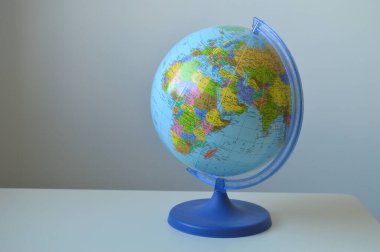 Kıtaları ve ulusal sınırları açıkça gösteren canlı, mavi bir siyasi küre, basit bir arkaplana karşı duruyor. Bu resim küresel çalışmalar, seyahat, eğitim, haritacılık ve uluslararası ilişkileri sembolize etmektedir.