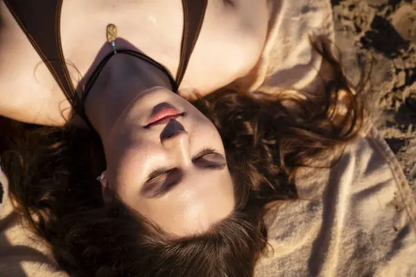 Genç bir kadın kumların üzerinde yatıyor..