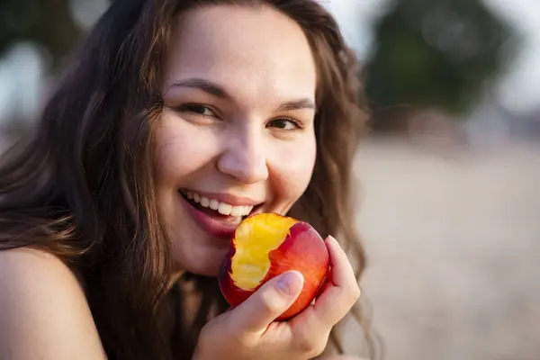 Kumsalda elinde kırmızı elmayla genç ve mutlu bir kadın.