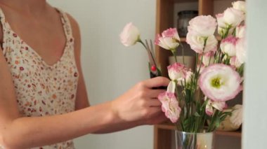 Elinde güllerle çiçek buketi tutan kadın. Çiçekçi çiçekleri budar. Vazoda güzel bir kompozisyon. Pembe çiçekler. Güzel kız. Hediye. Pastel renkler. Güzel bir iç mekan. Pembe güller. Eustoma. Şeffaf vazo. Sevgi. Yeşil. Makas.