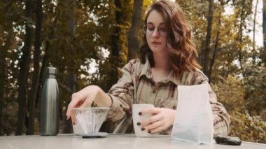 Parkta oturan genç bir kadın. Pişirme filtresi kahve