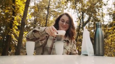 Beyaz kazaklı ve şapkalı genç bir kız sonbahar parkında kahve içiyor. Sonbahar havası. Pişirme filtresi kahve