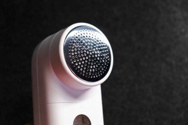 Kıyafetleri topaklardan temizlemek için bir cihaz. Ev için akıllı cihaz. Pudralık. - Beyaz. Karanlık arka plan. Ürün çekimi. Ellerde. Pelletler