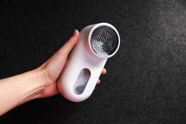 Kıyafetleri topaklardan temizlemek için bir cihaz. Ev için akıllı cihaz. Pudralık. - Beyaz. Karanlık arka plan. Ürün çekimi. Ellerde. Pelletler