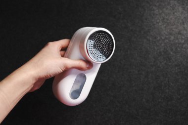 Kıyafetleri topaklardan temizlemek için bir cihaz. Ev için akıllı cihaz. Pudralık. - Beyaz. Karanlık arka plan. Ürün çekimi. Ellerde. Pelletler