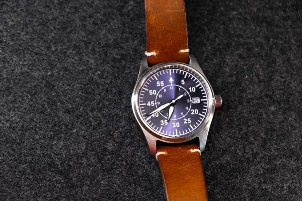 Deri kayışlı bir kol saati. Mekanik saat. Kahverengi kayış. Mor düğme. Erkek aksesuarı. Karanlık arka plan. Ürün çekimi