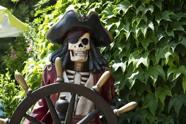 Siyah kafatası ve siyah şapkası olan tahta bir bankta bahçede korsan kafatası.