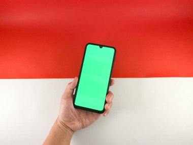 Bir el ele tutuşmayı yakın plan yapın ve cep telefonuna kırmızı ve beyaz arka planda yeşil ekranlı bir jest yapın ya da Endonezya bayrağı. Endonezya 'nın bağımsızlık günü tanıtımında kullanılabilir