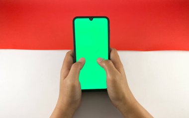 Bir el ele tutuşmayı yakın plan yapın ve cep telefonuna kırmızı ve beyaz arka planda yeşil ekranlı bir jest yapın ya da Endonezya bayrağı. Endonezya 'nın bağımsızlık günü tanıtımında kullanılabilir