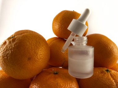 Portakal yığını üzerine bir şişe portakal renkli sıvı serum yakın plan. Şişenin bir damlası ve parlak gümüş bir kapağı var. Kozmetik veya cilt bakımı için kullanılabilir.. 